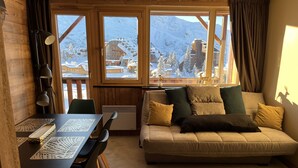 A cozy room with a wooden interior, a sofa with cushions, a table with a laptop, and a view of snow-covered mountains. - Resort center, app. 36 m2, 1 bedroom, mountain corner, balcony, ski room, WIFI (Morzine)