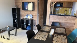 A modern living room with a dining area, wooden walls, a flat-screen TV, and a kitchen with yellow tiles. - Resort center, app. 36 m2, 1 bedroom, mountain corner, balcony, ski room, WIFI (Morzine)