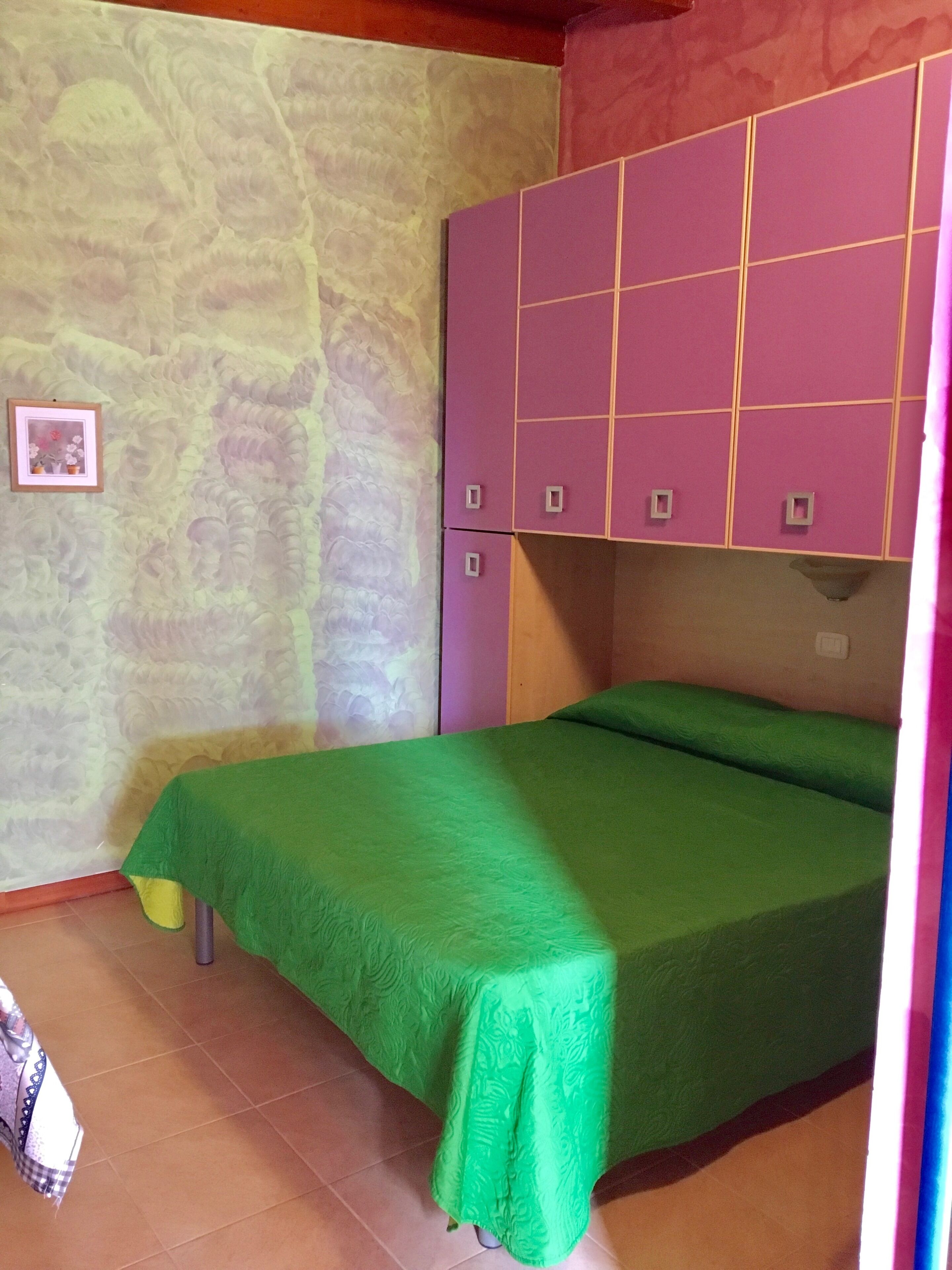 Una habitación con una cama verde, armarios morados y una pared con diseño de piedra.