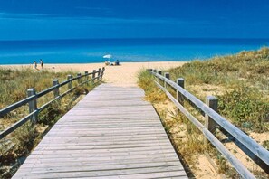 A wooden boardwalk leading to a beach with a clear blue sky.