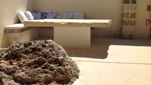 A stone bench with cushions, a tiled floor, and a stone wall.