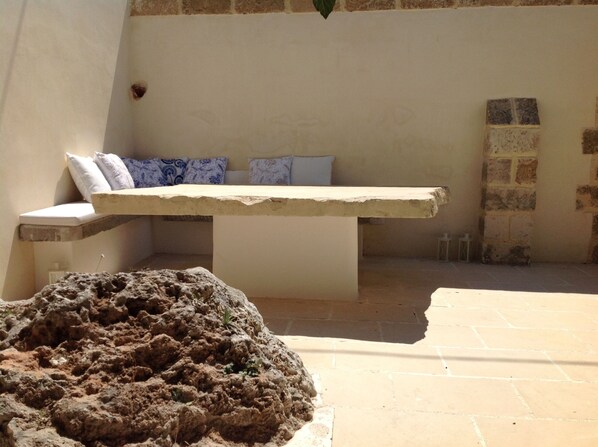 A stone bench with cushions, a tiled floor, and a stone wall.