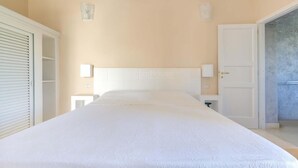 A bedroom with a large bed, a wardrobe, a nightstand, and a door leading to another room.