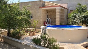 A swimming pool with a ladder, surrounded by a landscaped garden with various plants and a stone pathway.