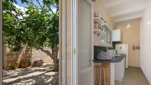 A compact kitchen with a small dining area, a refrigerator, and a window overlooking a courtyard with potted plants and a tree.