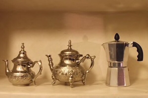 Three silver teapots of varying designs on a shelf.