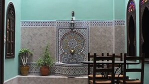 A Moroccan-style interior with a tiled fountain, wooden furniture, and decorative arches.
