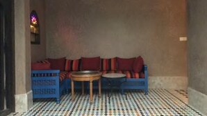 A room with a checkered floor, a blue sofa with red cushions, and a small round table.