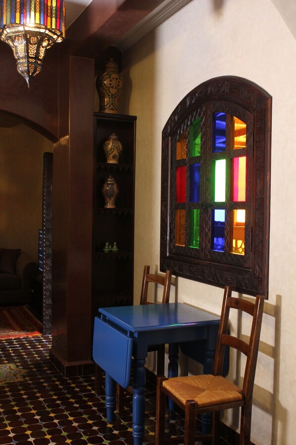 A room with a wooden table, chairs, a blue cabinet, a decorative shelf with vases, and a stained glass window.