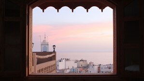 Une vue à travers une fenêtre ornée d’un cadre décoratif, donnant sur une ville côtière avec ses bâtiments et un imposant dôme.