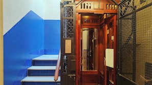 Una escalera con paredes de azulejos azules, una puerta de madera con celosía metálica y una pared blanca con una puerta.