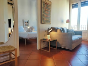 A room with a bed, a sofa, a small table with a lamp, and a poster on the wall.