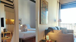 Habitación de hotel con cama, sofá, una mesita de noche con lámpara, un cuadro en la pared y ventana con vistas.