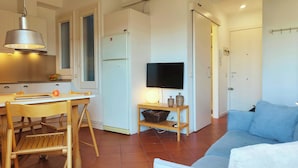 Un espacio habitable compacto con kitchenette, zona de comedor, televisor montado en la pared y sofá.