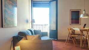 Una sala de estar con un sofá, una mesa de comedor con sillas, una computadora portátil y un cuadro en la pared.