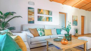 A living room with a sofa, coffee table, and various cushions. There are paintings on the wall and a plant on the floor. - SON LLANERAS VILLA - NEAR ES TRENC, MALLORCA, RELAXING GETAWAY, POOL, A/C, WIFI (Campos)