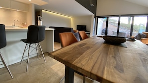 Une cuisine moderne avec un coin repas, comprenant une table et des chaises en bois, une grande fenêtre donnant sur l’extérieur et un four encastré.