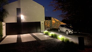 Une maison moderne à deux étages, dotée d’un garage, d’une allée et d’une voiture garée devant.