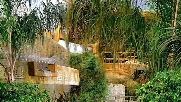 Un toboggan aquatique où des personnes dévalent la pente à l’intérieur de bouées gonflables, le tout entouré d’une végétation luxuriante et de structures en pierre.