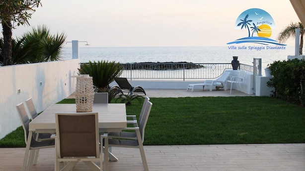 An outdoor patio with a table and chairs, a grassy area, and a view of the sea. - Villa on the Diamante beach  (Belvedere Marittimo)