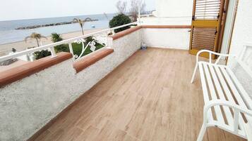 Ein Balkon mit Blick auf das Meer, weiße Stühle und eine Holztür.