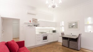 A modern kitchen with white cabinetry, a dining area with a table and chairs, and a red sofa in the foreground. - Luxury apartment in the heart of Rome - Spanish Steps, wi-fi, a / c, (Roma)