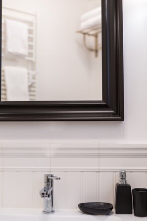 Un baño con pared de azulejos blancos, espejo de marco negro, grifo cromado, dispensador de jabón negro y taza negra.