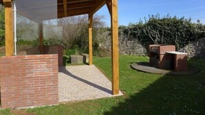 Un'area esterna riparata con struttura in mattoni, travi in legno e un barbecue in muratura.