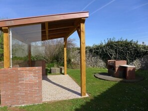 Un espacio al aire libre techado con una estructura de ladrillo, vigas de madera y una parrilla de ladrillo.