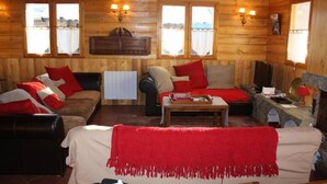A cozy cabin interior with wooden walls, a sofa set, a dining table, and two windows with curtains. - Chalet in wood and stone, redone, 250 metres from the ski lifts. (Les Deux-Alpes)