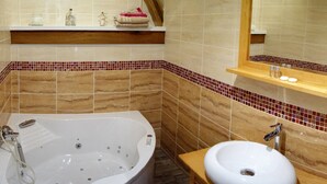 A bathroom with a bathtub, a sink, and a mirror. There are shelves with toiletries and a wooden shelf above the bathtub.