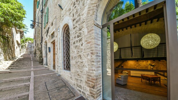 A narrow street with stone buildings, a wooden staircase, and a restaurant with a modern interior and large windows. - Loft in the center of Assisi (Assisi)