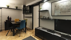 Een moderne woonkamer met een eethoek, een flatscreen televisie en een wandplank met decoratieve objecten.