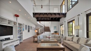 Un vaste salon doté d’un haut plafond, d’un escalier menant à l’étage supérieur et d’un grand téléviseur à écran plat placé sur le côté gauche.