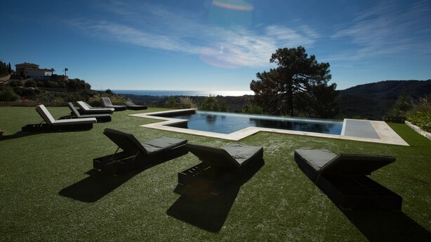Un espace aménagé au bord de la piscine, avec plusieurs chaises longues et une piscine, le tout entouré d’une pelouse bien entretenue et offrant une vue sur l’océan.
