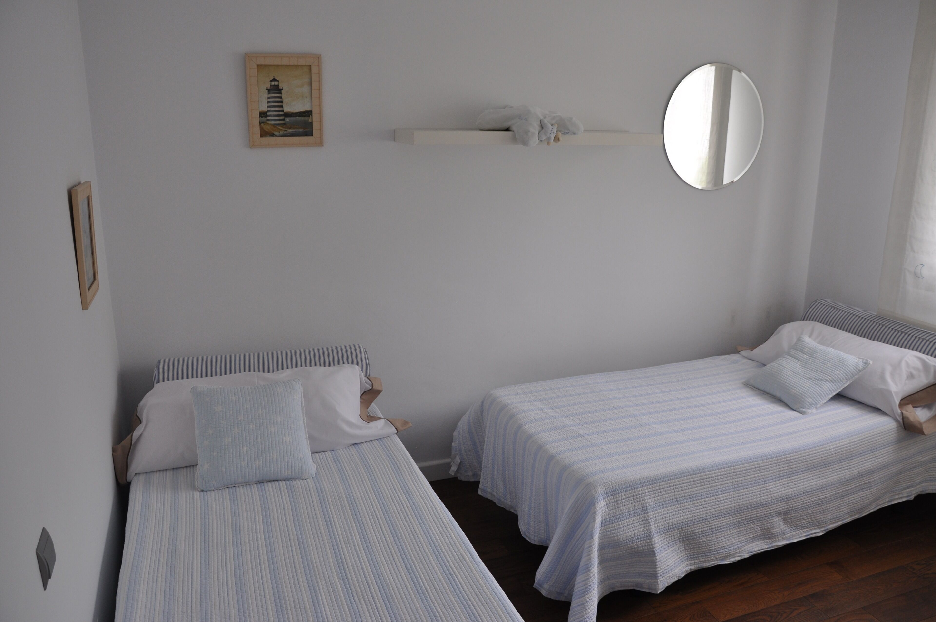 Een slaapkamer met twee eenpersoonsbedden, een nachtkastje, een spiegel en een ingelijst kunstwerk aan de muur.