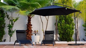 Een terras met twee stoelen en een tafel, een zwarte parasol en een palmboom.
