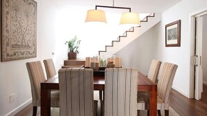 Een eethoek met een houten tafel, gestreepte stoelen, een trap en een hanglamp.