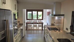 Een moderne keuken met roestvrijstalen apparatuur, een eethoek met een tafel en stoelen, en een groot raam dat zorgt voor natuurlijk licht.