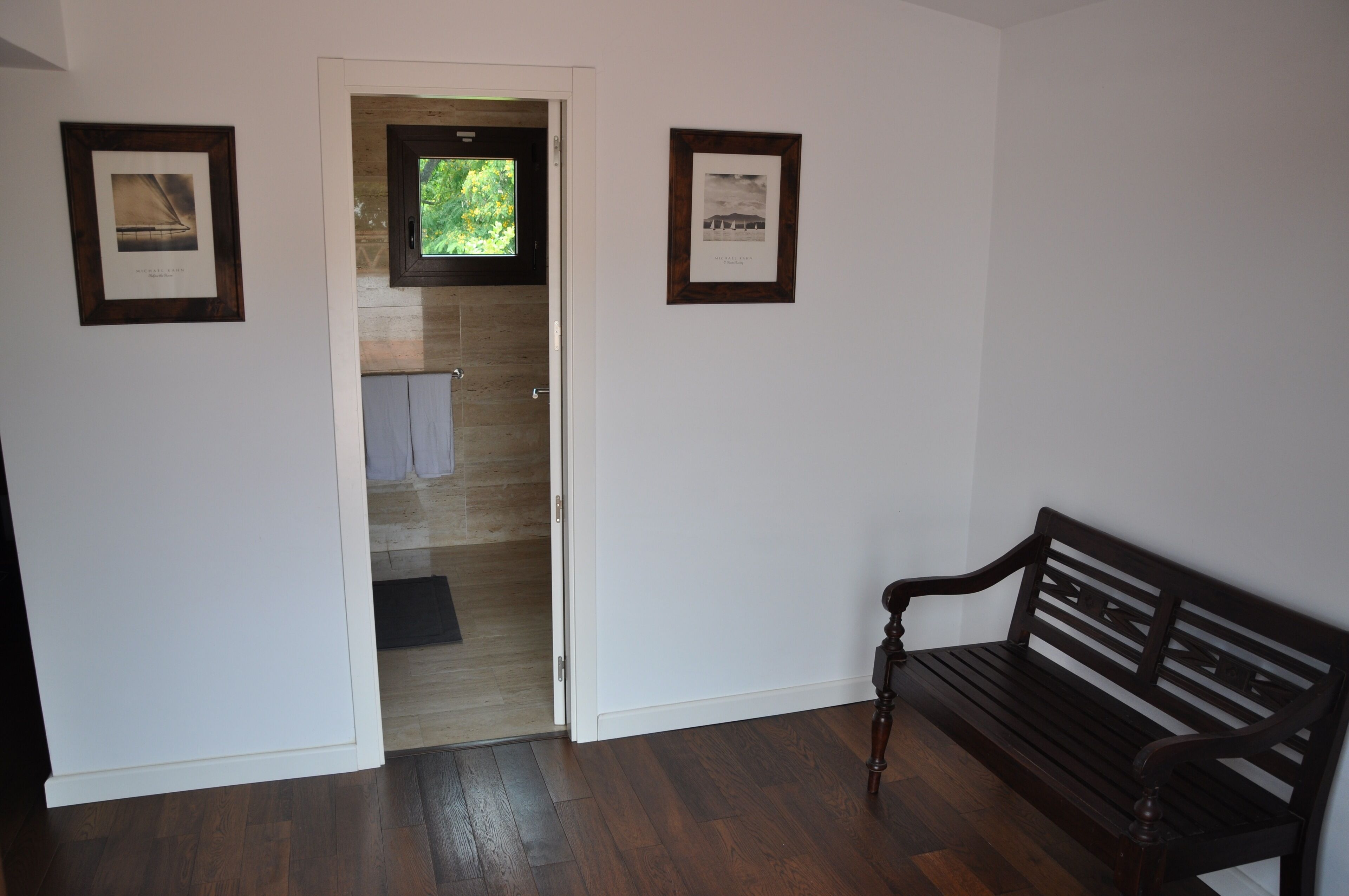 Un pasillo con un banco de madera, una puerta que da a un baño y dos cuadros en las paredes.