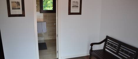 Un pasillo con un banco de madera, una puerta que da a un baño y dos cuadros en las paredes.