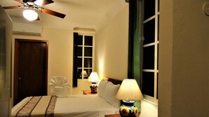 A hotel room with a bed, a nightstand with a lamp, a ceiling fan, and a window with curtains. - Cozy Studio for 2 pers. near 5th avenue (Playa del Carmen)
