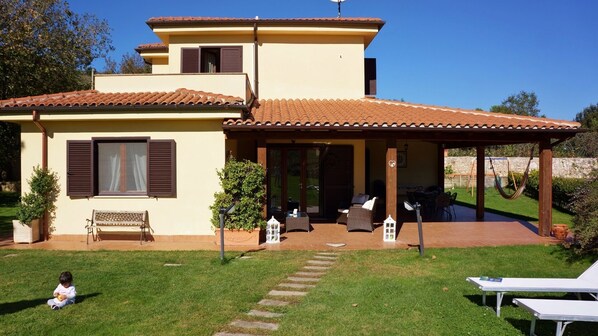 Una casa de dos pisos con un patio, un banco y mobiliario exterior.