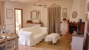 Een gezellige woonkamer met een witte bank, een klein tafeltje, een open haard en een klok aan de muur.