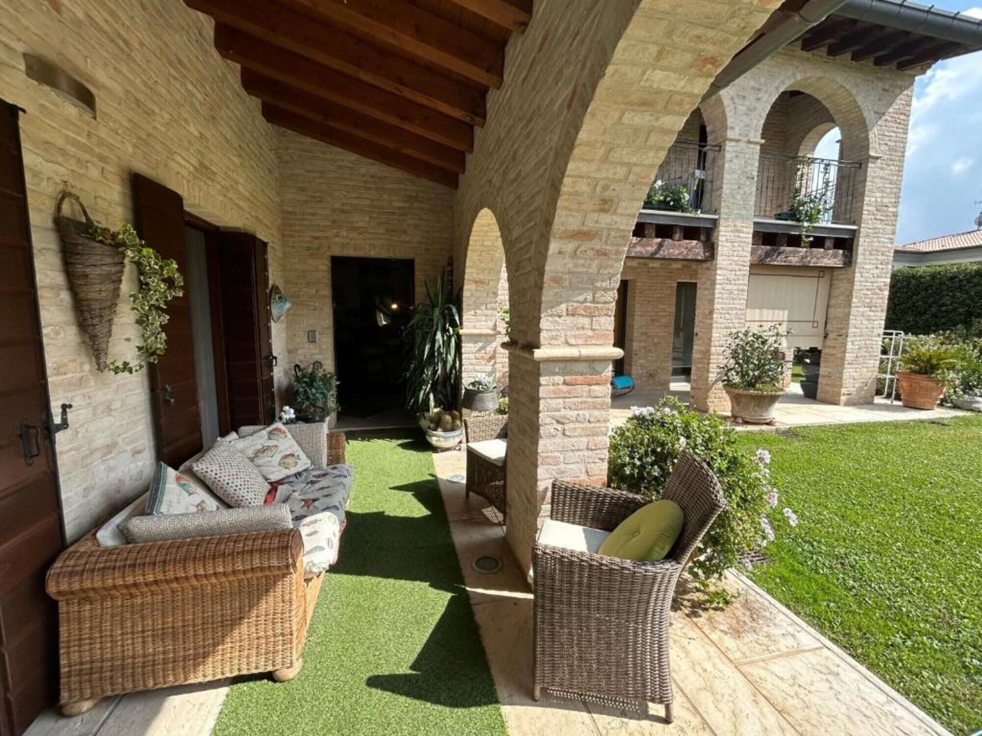 Eine Terrasss mit Korbmöbeln, synthetischem Rasen und Topfpflanzen.