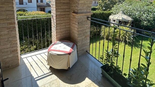 A balcony with a small table and chair, stone walls, and a view of a garden and houses. - Welcome to White Lady (Portogruaro)