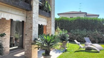 Un edificio a due piani con un balcone, un giardino con prato e piante in vaso, e una poltrona da relax.