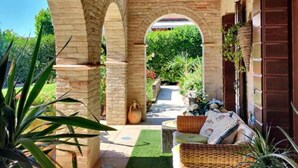 A covered patio with brick arches, a wicker sofa, and a small garden area. - Welcome to White Lady (Portogruaro)