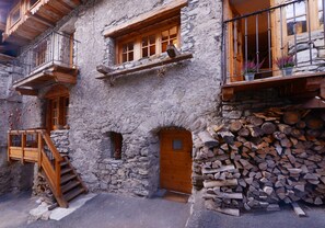 A rustic stone building with wooden balconies, a wooden staircase, and a door. - Chalet ALOUETTE RARE confort 4* La Plagne Champagny proche Pistes Shops (CHAMPAGNY en VANOISE)