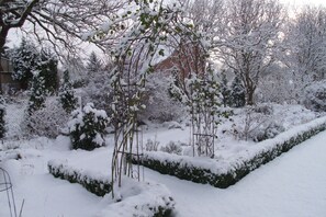 A snow-covered garden with a hedge and trees.